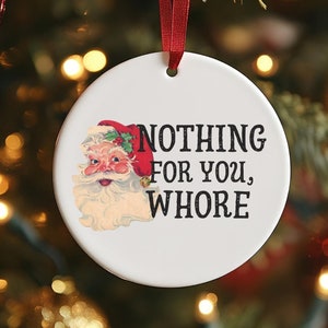 May include: A white ceramic Christmas ornament with a cartoon image of Santa Claus and the text "NOTHING FOR YOU, WHORE".