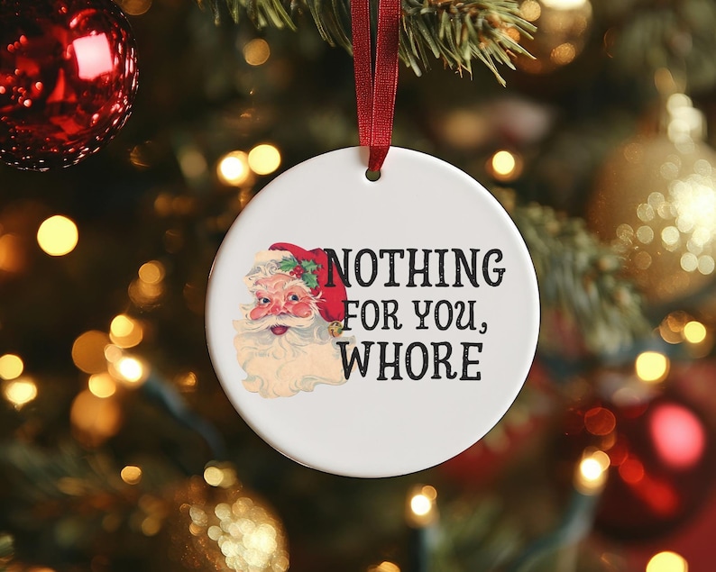 May include: A white ceramic Christmas ornament with a cartoon image of Santa Claus and the text "NOTHING FOR YOU, WHORE".