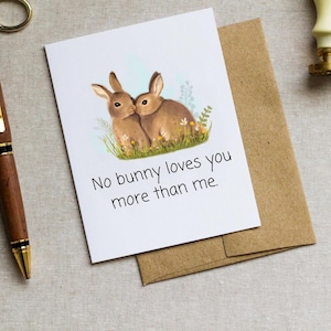 May include: A white card with a watercolor illustration of two brown bunnies cuddling. The card has the text "No bunny loves you more than me."
