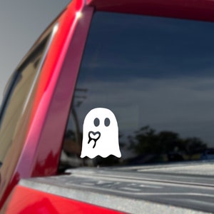 May include: White ghost sticker with a tooth and heart inside, on a red truck tailgate.