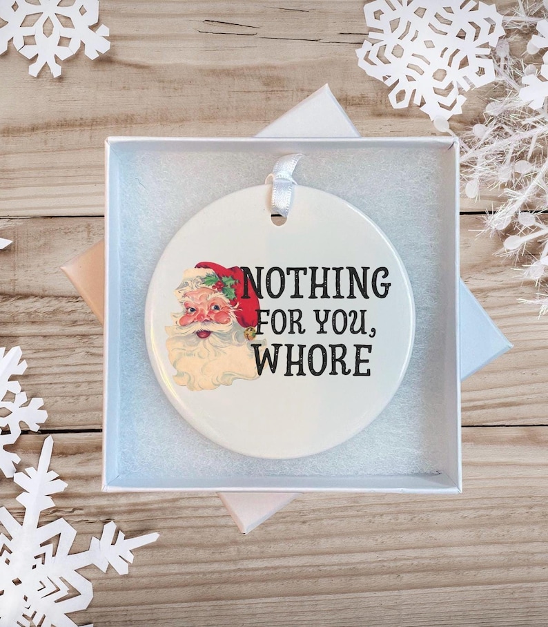 May include: White ceramic Christmas ornament with a cartoon image of Santa Claus and the text "NOTHING FOR YOU, WHORE".