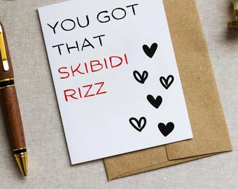 May include: White card with black text that reads "You got that Skibidi Rizz" with several black hearts drawn around the text.
