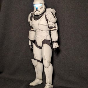 May include: A white action figure of a Star Wars Stormtrooper wearing a white helmet with a blue visor. The figure is standing on a black surface.