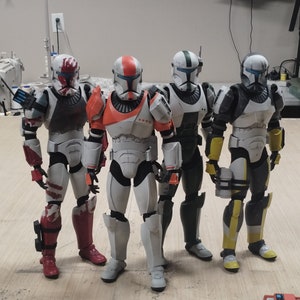 Puede incluir: Cuatro figuras de acción de soldados clon con varios diseños de armadura. Las figuras son principalmente blancas con detalles en rojo, naranja, negro y amarillo. Cada figura tiene un diseño de casco único y está de pie.