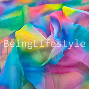 May include: A vibrant, flowing fabric in a rainbow of colors, including pink, yellow, green, and blue. The text "BeingLifestyle" is printed on the fabric. The material appears to be lightweight and translucent, with soft folds and a delicate texture.