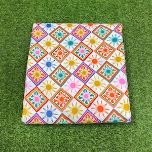 Peut inclure: Tissu plié avec un motif géométrique répétitif de losanges et d'éclairs colorés. Le motif présente des éléments orange, sarcelle, rose, jaune et bleu sur un fond blanc. Le tissu est probablement en coton ou dans une matière similaire.