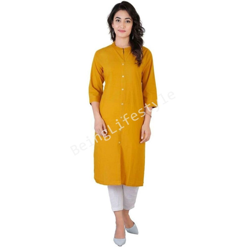 May include: A mustard yellow long-sleeved button-down top with a mandarin collar. The top is knee-length and has a straight fit.