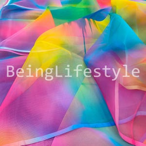 May include: A vibrant, multi-colored fabric with a rainbow gradient of pink, yellow, blue, and green hues. The text "BeingLifestyle" is displayed across the fabric. The material appears to be lightweight and flowing, with a translucent quality.