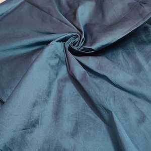 以下が含まれることがあります： 滑らかで絹のような質感のターコイズブルーの生地のクローズアップ。生地は折り畳まれ、ドレープされており、その柔らかく流れるような性質を示しています。