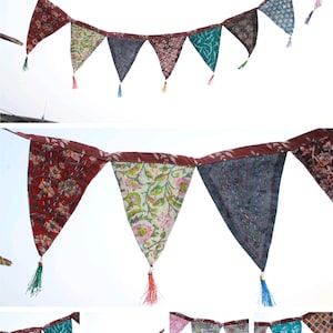 May include: A colourful fabric bunting with triangular flags featuring various floral and geometric patterns. Each flag has a tassel at the bottom.