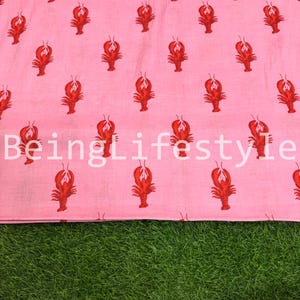 Puede incluir: Tela rosa con un patr&oacute;n repetido de langostas rojas. El texto blanco "BeingLifestyle" est&aacute; impreso en la tela. La tela se muestra sobre una superficie verde.