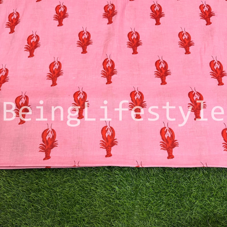 Puede incluir: Tela rosa con un patr&oacute;n repetido de langostas rojas. El texto blanco "BeingLifestyle" est&aacute; impreso en la tela. La tela se muestra sobre una superficie verde.