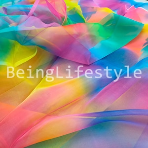 May include: A vibrant, multi-colored fabric with a rainbow gradient of colors including pink, yellow, green, and blue. The text "BeingLifestyle" is displayed in white across the fabric. The fabric appears to be lightweight and flowing.