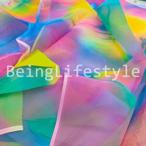 May include: A vibrant fabric with a rainbow gradient of colors, including pink, yellow, green, and blue. The text "BeingLifestyle" is printed on the fabric. The material appears to be lightweight and sheer.