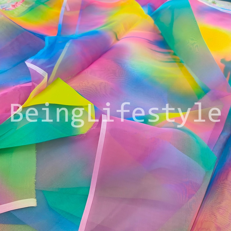 May include: A vibrant fabric with a rainbow gradient of colors, including pink, yellow, green, and blue. The text "BeingLifestyle" is printed on the fabric. The material appears to be lightweight and sheer.