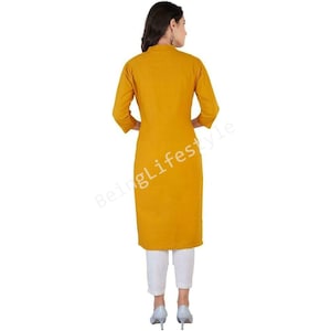 May include: A mustard yellow long-sleeved kurta with a mandarin collar. The kurta is knee-length and has a straight fit. The model is wearing white pants and gray heels.