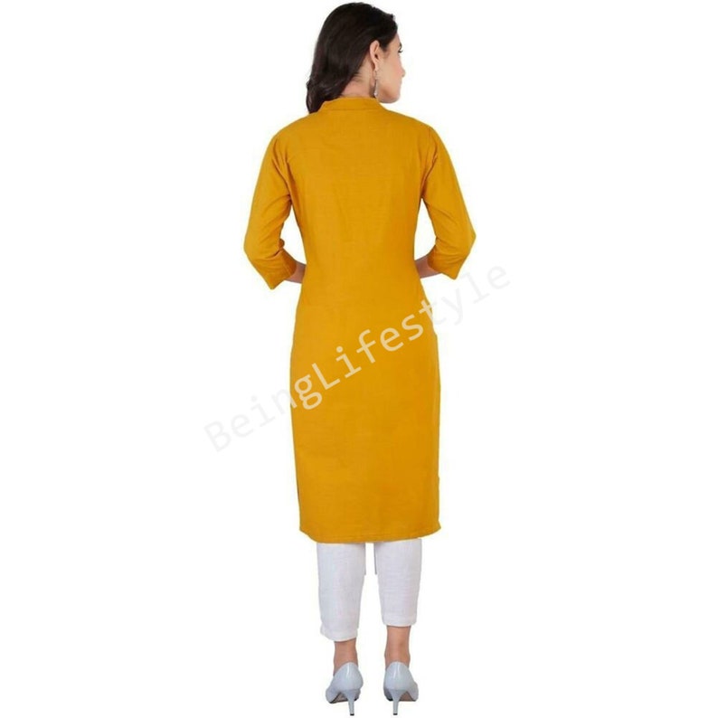 May include: A mustard yellow long-sleeved kurta with a mandarin collar. The kurta is knee-length and has a straight fit. The model is wearing white pants and gray heels.