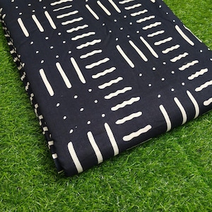 Op de afbeelding: Een opgevouwen stuk donker marineblauwe stof met een herhalend patroon van witte verticale lijnen, golvende lijnen en stippen. De stof wordt gepresenteerd op een bed van groen gras.