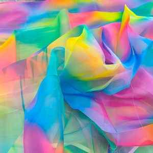 May include: A vibrant, multi-colored fabric with a rainbow gradient effect. The sheer material displays a blend of bright hues, including yellow, blue, pink, and green, creating a flowing, ethereal appearance. The fabric is likely used for decorative purposes.