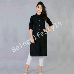 May include: A black long-sleeved collared shirt with a button-up front and gold buttons. The shirt has a slightly fitted silhouette and is worn with white trousers.