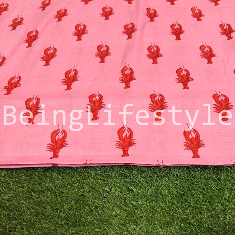 Puede incluir: Tela rosa con un patr&oacute;n repetido de langostas rojas. El texto "BeingLifestyle" est&aacute; impreso en blanco en la tela. La tela se muestra sobre una superficie verde.