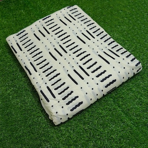 May include: Folded cream fabric featuring a repeating pattern of black lines and dots. The design incorporates straight and wavy lines, creating a geometric aesthetic. The fabric is displayed on a green surface.