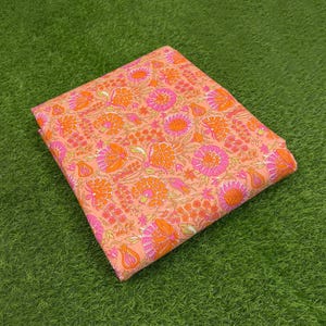 May include: A square piece of folded fabric featuring a repeating floral pattern in shades of bright orange, soft pink, and light peach. The design consists of various stylized flower heads, small buds, and leafy stems arranged across the surface.