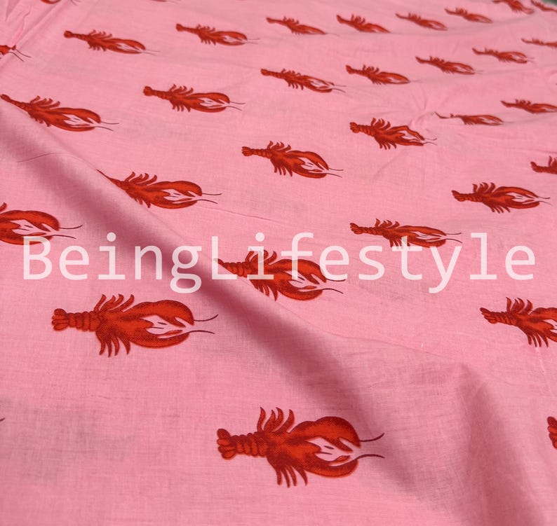 Puede incluir: Tela rosa claro con un patr&oacute;n repetido de langostas rojas. El texto "BeingLifestyle" est&aacute; impreso en la tela. La tela parece ser de algod&oacute;n, adecuada para varios proyectos de costura.