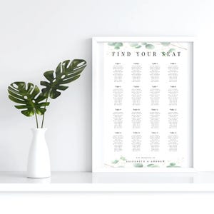 May include: A white framed wedding seating chart with a green and white floral design. The chart is titled "Find Your Seat" and lists the names of guests assigned to each table. The bottom of the chart reads "The Wedding of Elizabeth & Andrew".