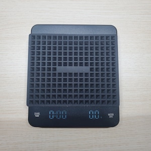 May include: Black digital kitchen scale with a textured black surface. The scale has a digital display showing "0:00" and "00."