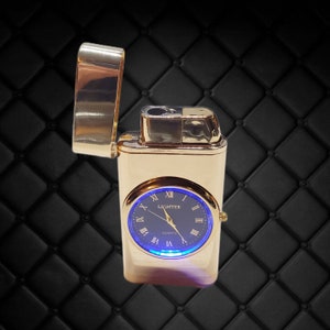 May include: Gold-colored lighter with a built-in watch. The watch face is dark blue with Roman numerals and the word "Lighter" above the hands. The lighter's lid is open, and the watch has a blue light around the face.