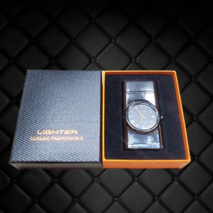 May include: A black and silver lighter with a watch face on the front. The lighter is in a black and orange box with the words "LIGHTER CLASSIC FASHIONABLE" printed on the box.