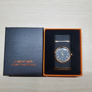 May include: A black lighter with a gold trim and a watch face that says "QUARTZ" on it. The lighter is in a black box with the words "LIGHTER CLASSIC FASHIONABLE" on it.
