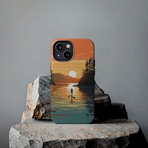May include: A phone case with a sunset scene featuring a silhouette of a person paddleboarding on a lake. The case has a dark blue, teal, and orange color scheme.