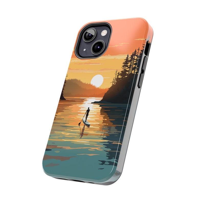May include: A phone case with a sunset scene featuring a person paddleboarding on a lake. The sky is orange and pink, and the water is blue and green. There are trees on the shore.