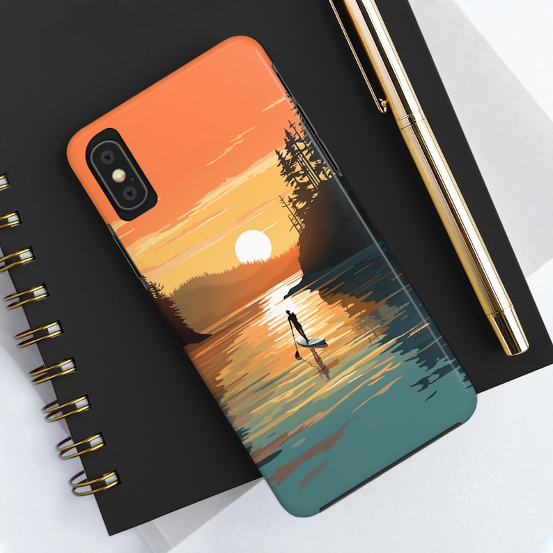 May include: A phone case with a sunset scene over a lake. The sun is setting behind a forested shoreline, and a person is paddleboarding in the water. The sky is a gradient of orange, yellow, and pink.