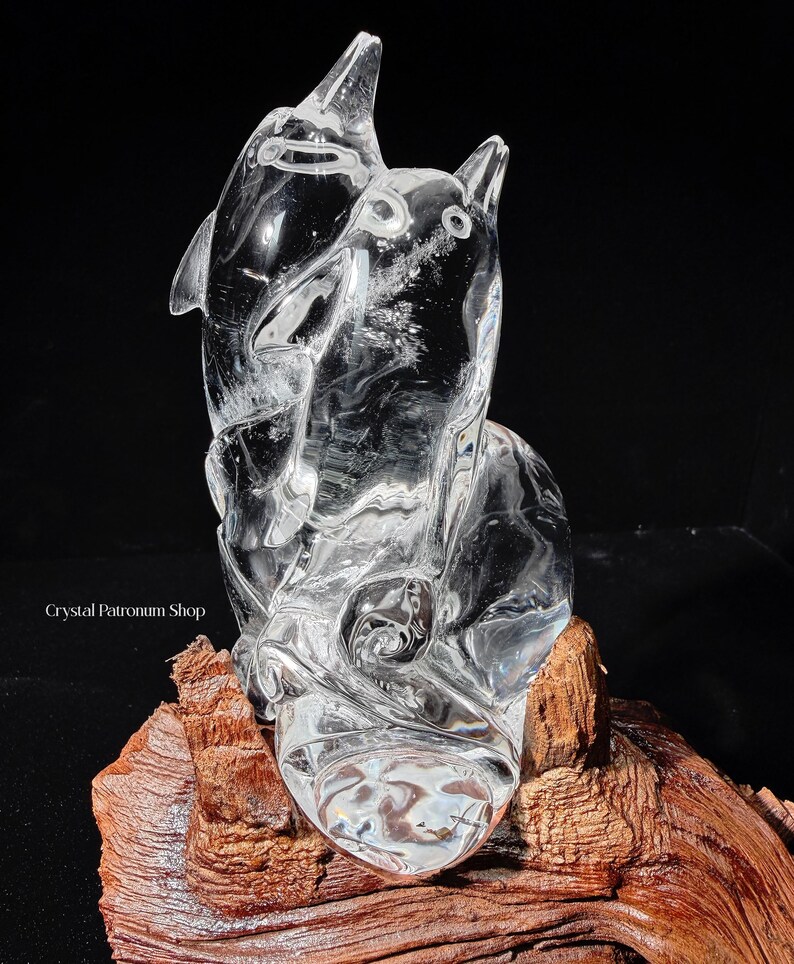 Pode incluir: Uma escultura de cristal transparente de dois golfinhos, um saltando para cima, o outro olhando. A escultura &eacute; montada em um peda&ccedil;o de madeira natural. A imagem est&aacute; em um fundo preto.