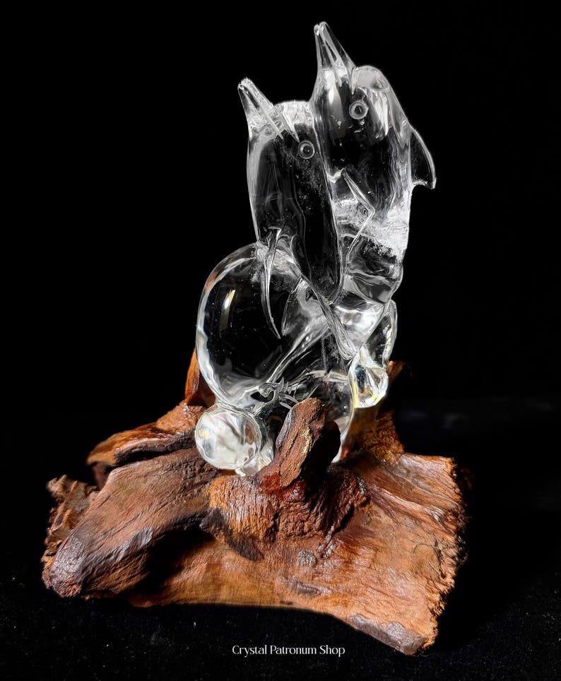 Pode incluir: Uma escultura de cristal transparente de dois golfinhos estilizados, montada sobre um peda&ccedil;o de madeira flutuante natural marrom escuro. Os golfinhos s&atilde;o esculpidos de forma intrincada com formas lisas e arredondadas e barbatanas pontiagudas. O conjunto est&aacute; sobre fundo preto.