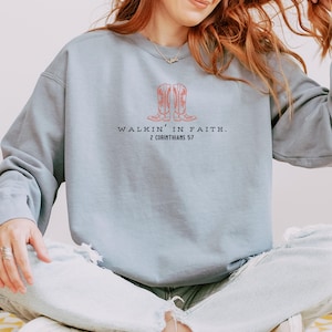 May include: A light blue sweatshirt with a graphic of two cowboy boots and the text "Walkin' in Faith. 2 Corinthians 5:7"