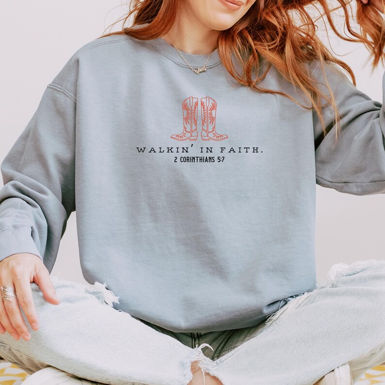 May include: A light blue sweatshirt with a graphic of two cowboy boots and the text "Walkin' in Faith. 2 Corinthians 5:7"