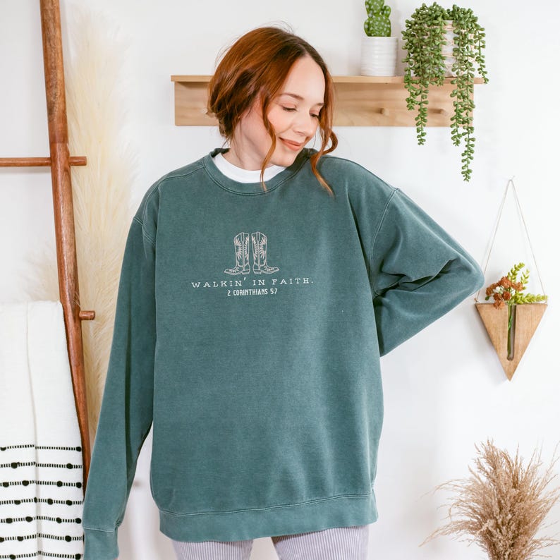 May include: A teal green sweatshirt with a white graphic of cowboy boots and the text "Walkin' in Faith. 2 Corinthians 5:7"