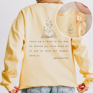 May include: Yellow sweatshirt featuring a quote about training up a child in the way they should go, even when they are old. The quote is from Proverbs 22:6. The sweatshirt also has a drawing of an open book with flowers and paper aeroplanes coming out of it.