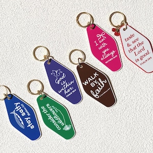 May include: A collection of colorful keychains with gold rings. Each keychain features a different color and a unique message, including phrases like "Stay Salty," "God is within her," and "Walk by Faith." The keychains are designed with a retro motel key style.