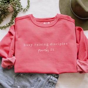May include: A pink sweatshirt with the text "busy raising disciples" and "Proverbs 22:6" in white lettering.