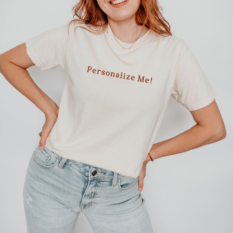 May include: A white t-shirt with the text "Personalize Me!" printed in brown on the front.