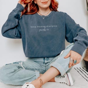 May include: A navy blue sweatshirt with the text "busy raising disciples proverbs 22:6" printed on the front.