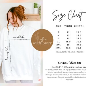 May include: Size chart for a white sweatshirt with the words "with a wildflower" printed on the front. The chart shows the width and length measurements in inches for sizes S through 3XL.