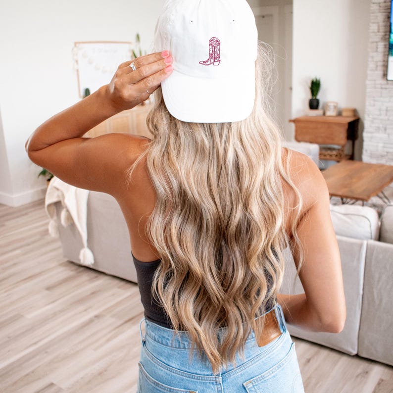 Pu&ograve; includere: Un cappello da baseball bianco con un design di stivale ricamato in bordeaux.