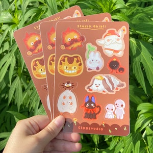 May include: Three sticker sheets featuring Studio Ghibli characters. Each sheet is brown with various colorful illustrations of characters from the animated films. The text "Studio Ghibli" and "Eloostudio" are printed on the sheets.