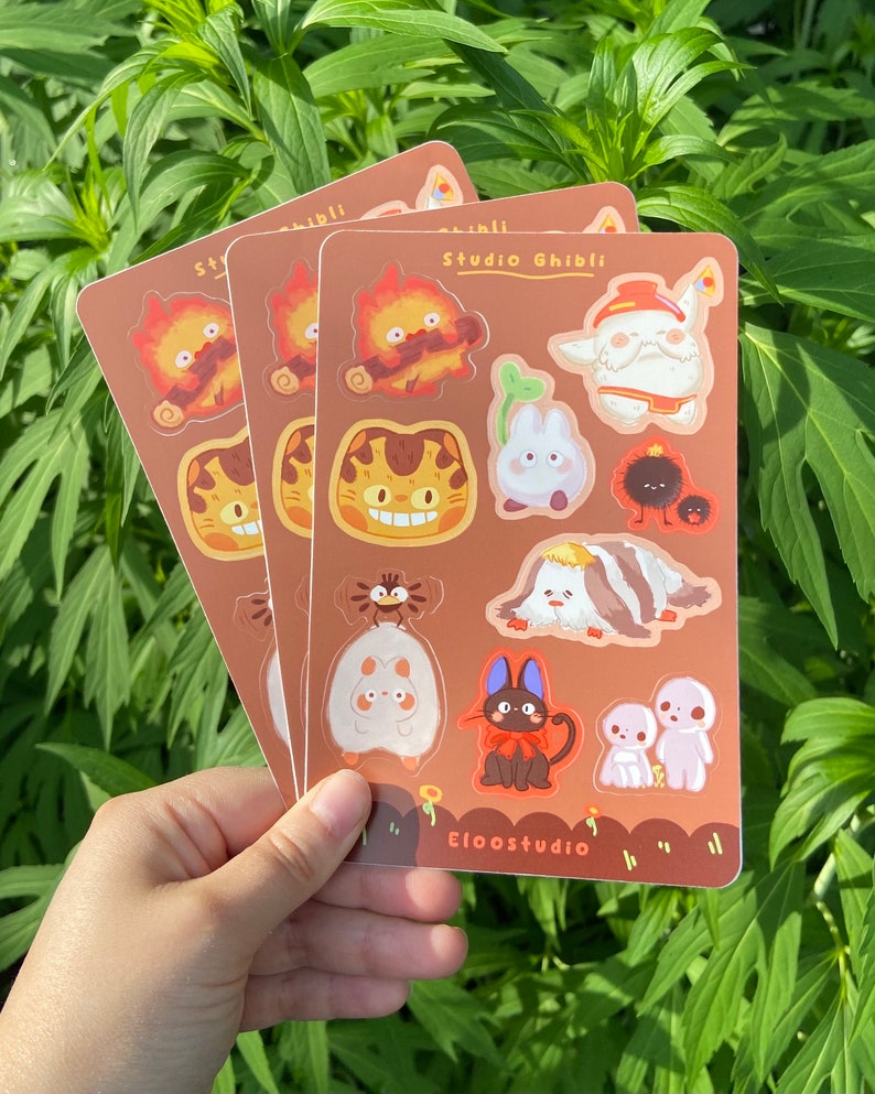 May include: Three sticker sheets featuring Studio Ghibli characters. Each sheet is brown with various colorful illustrations of characters from the animated films. The text "Studio Ghibli" and "Eloostudio" are printed on the sheets.